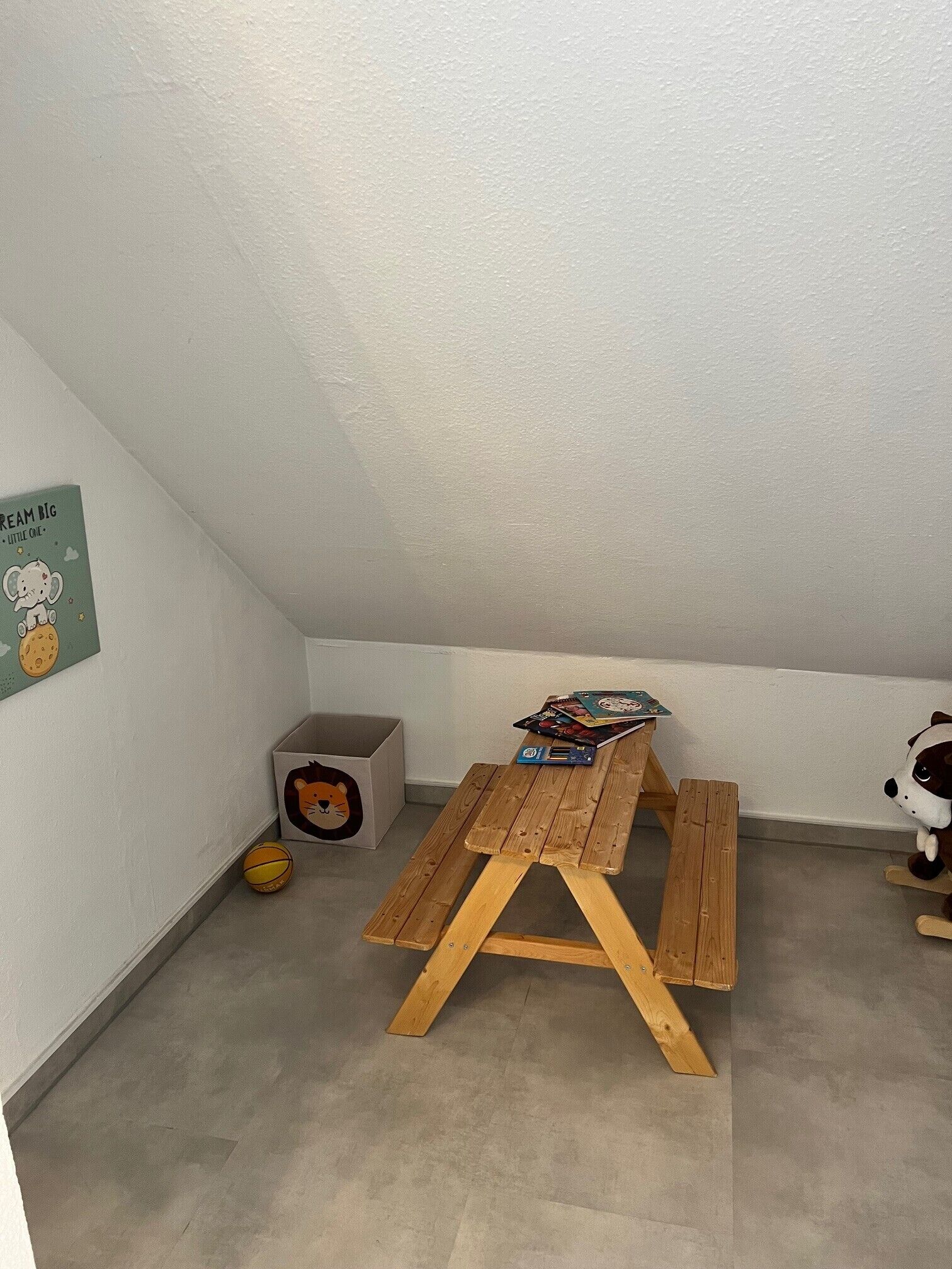 Ein kleiner Raum mit einem Holztisch, einer Bank, einem Basketball, einer Spielkiste und einem Stofftier.