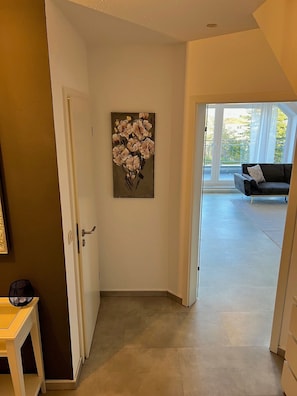 A hallway with a door leading to a living area, a painting on the wall, and a small table with a fan.