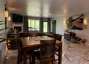 Un espace repas comprenant une table et des chaises en bois, un baby-foot et un coin bar avec un téléviseur.