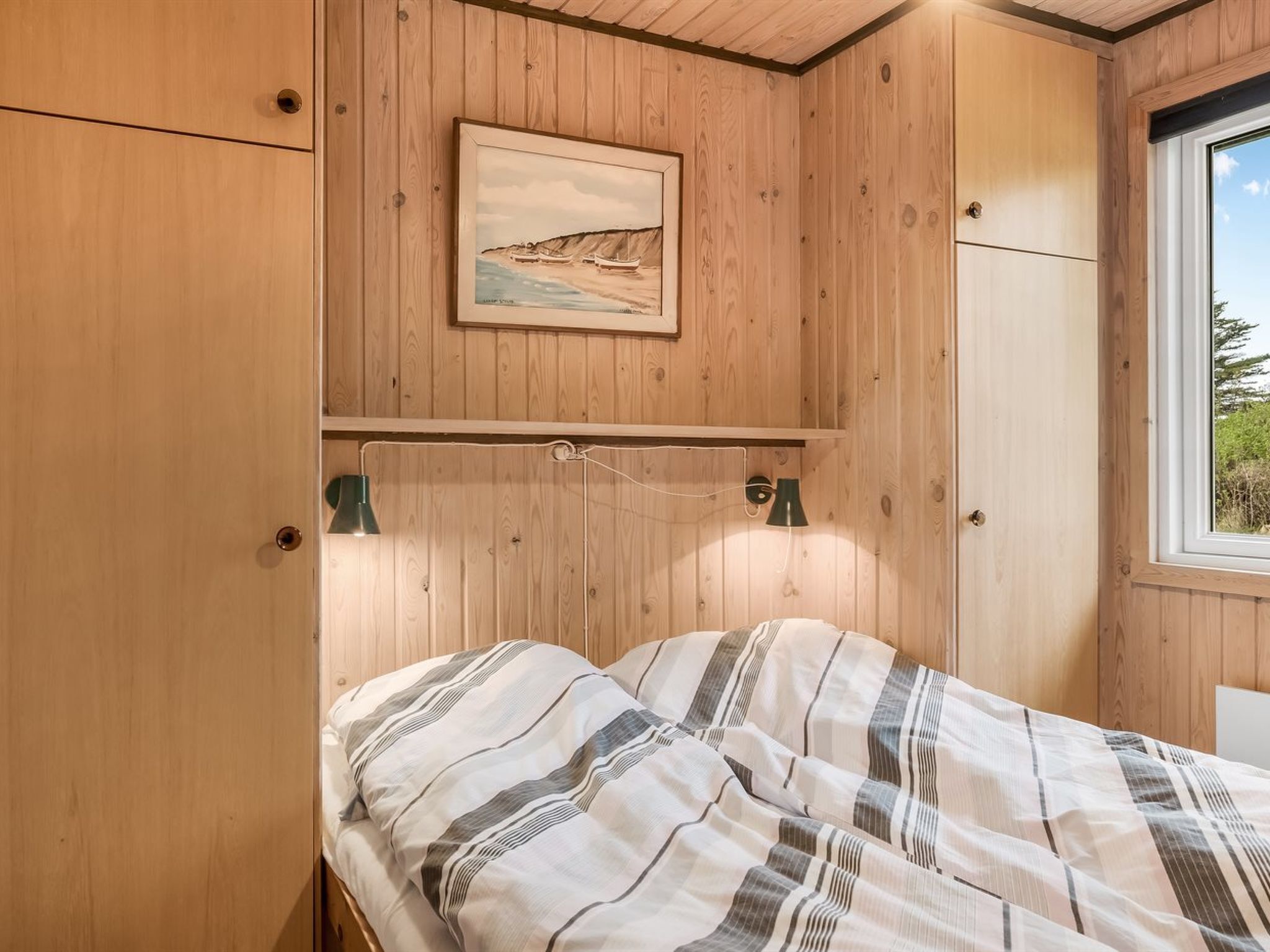 Habitación con paneles de madera, una cama, dos lámparas fijadas a la pared y un cuadro enmarcado sobre la cama.