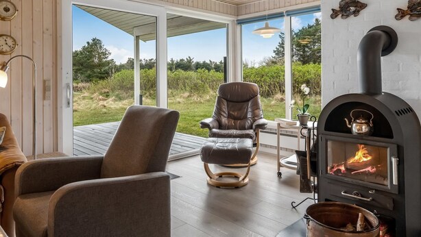 Ein modernes Wohnzimmer mit Kamin, Ledersesseln und einem großen Fenster mit Blick auf eine natürliche Landschaft.