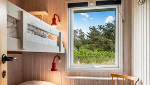 Ein kleines Zimmer mit Etagenbett, Schreibtisch, Stuhl und Fenster mit Blick auf Grünflächen.