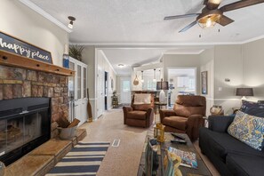 A living room with a fireplace, two brown armchairs, a black sofa, and a ceiling fan.