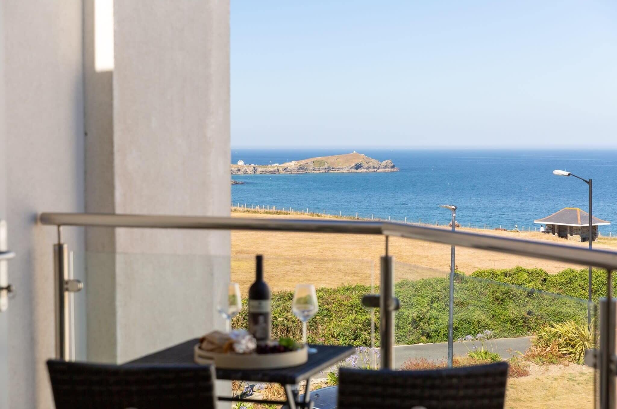 Balcón con mesa lista para comer, con vistas a la costa, una pequeña isla y el mar.