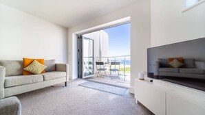 Un soggiorno moderno con divano, televisore a schermo piatto e balcone con tavolo e sedie.
