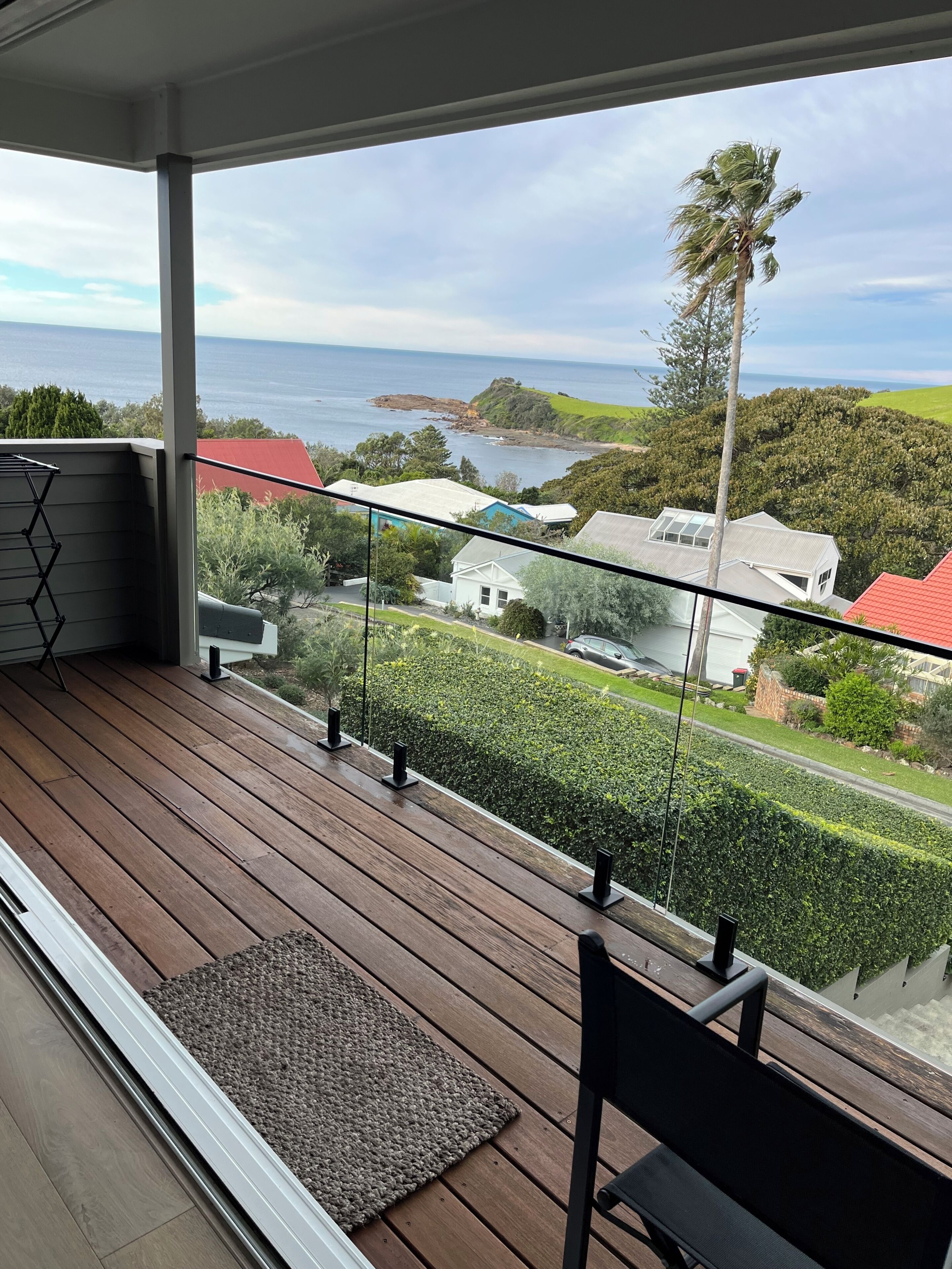 Un balcon avec vue sur la mer et les maisons, un plancher en bois et un banc.