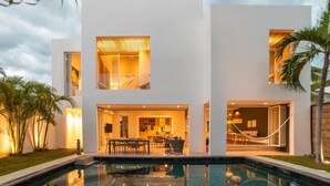 Ein modernes, zweistöckiges Haus mit Swimmingpool, Außenbereich zum Sitzen und einem gut beleuchteten Innenraum.