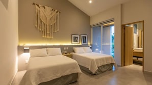 Ein modernes Schlafzimmer mit zwei Betten, einem Wandbehang aus Makramee, gerahmten Bildern und einer Glastür zum Balkon.