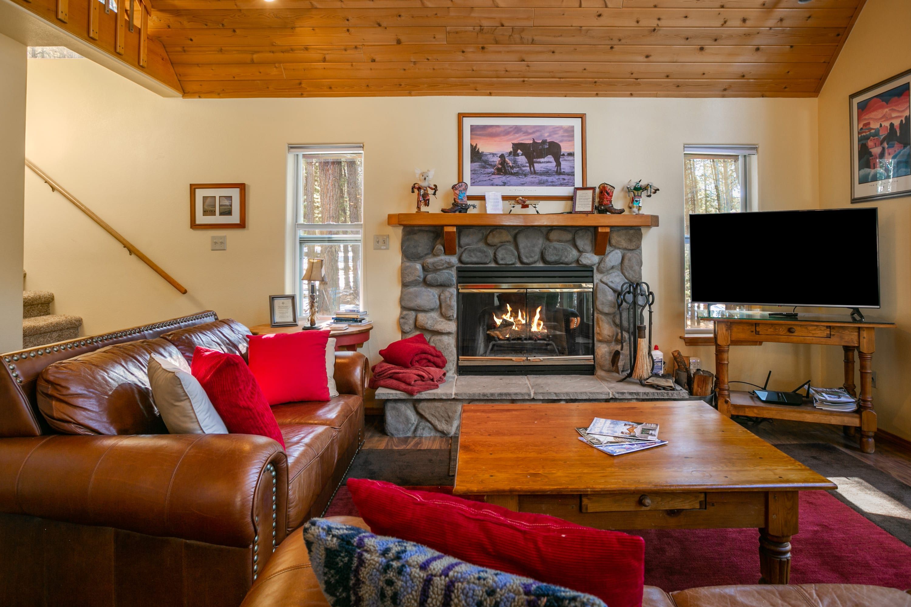 A cozy living room with a stone fireplace, leather sofa, and a flat-screen TV.