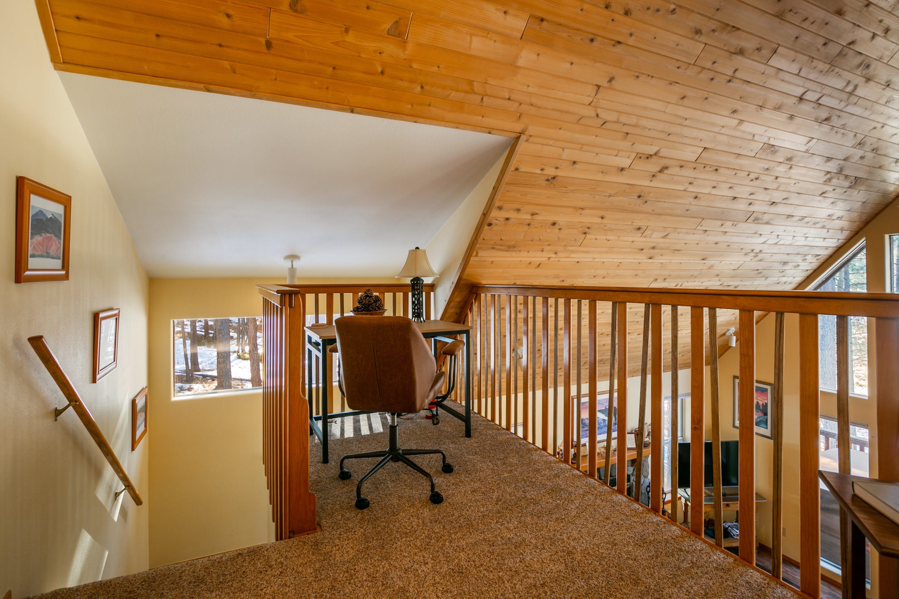 Una escalera de madera con vistas a una habitación que tiene un escritorio, una silla, una ventana y un cuadro en la pared.
