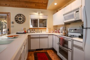 A modern kitchen with white cabinets, a clock, a window with blinds, and a microwave. - Memory Mtn Lodge by Velo (Angel Fire)