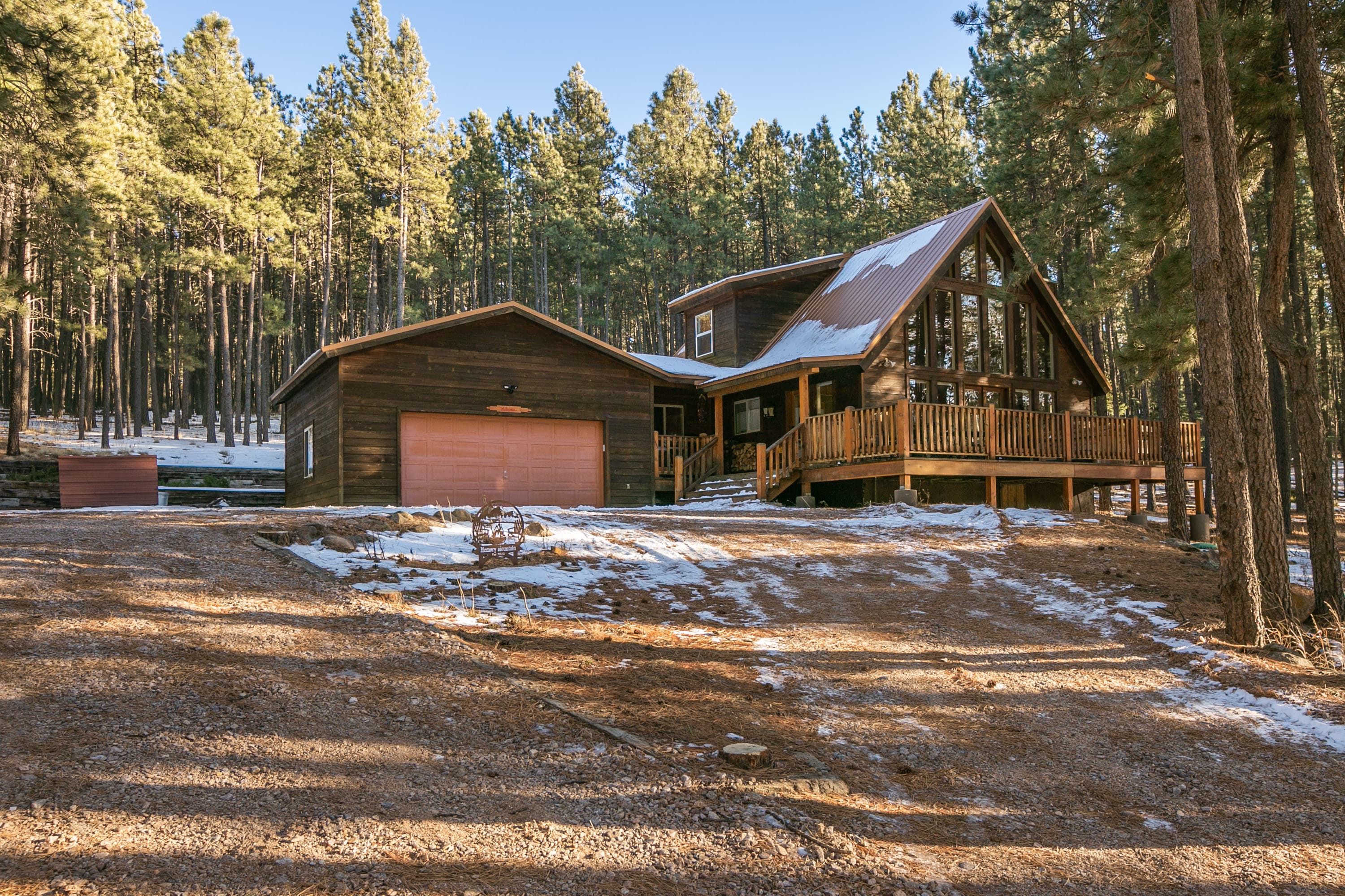 A cabin with a large garage, a deck, and a forested backdrop.