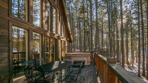 A wooden deck with a table and chairs, overlooking a forest. - Memory Mtn Lodge by Velo (Angel Fire)