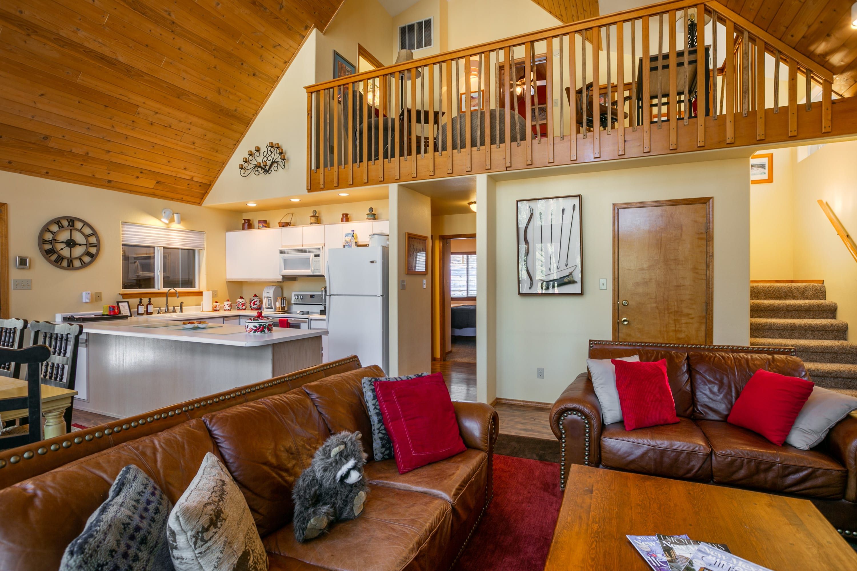 A spacious living area with a high ceiling, a kitchen with modern appliances, a dining area, and a staircase leading to an upper level.