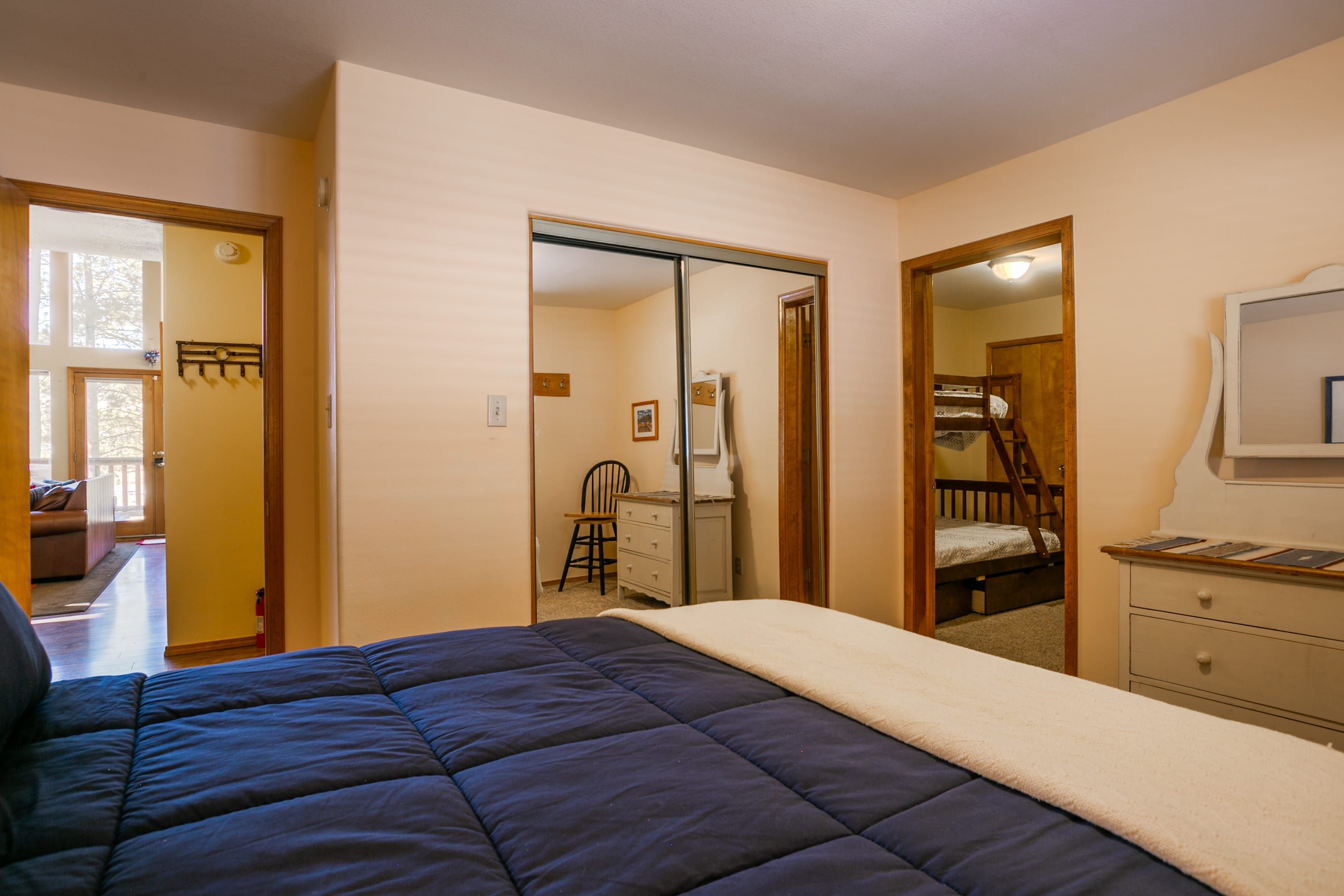 Een slaapkamer met een bed, een dressoir en een spiegel. Een deur leidt naar een andere kamer.
