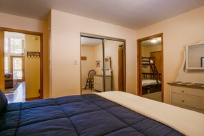 Een slaapkamer met een bed, een dressoir en een spiegel. Een deur leidt naar een andere kamer.