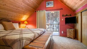 A bedroom with a bed, a nightstand, a lamp, a television, and a window with a view of trees. - Memory Mtn Lodge by Velo (Angel Fire)