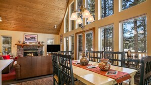 Una sala de estar acogedora con chimenea, techo de madera, ventanas amplias y un comedor con sillas y mesa.