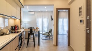 A modern kitchen with a dining area, a TV mounted on the wall, and a door leading to another room. - Pananos Sq House I (Heraklion)