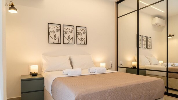 A modern hotel room with a large bed, bedside tables, wall art, and a mirror. - Pananos Sq House I (Heraklion)