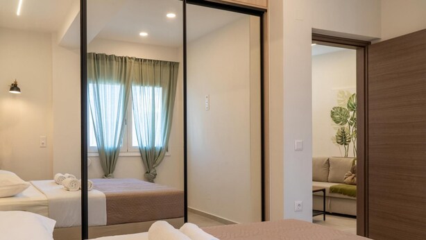 A hotel room with two beds, a large mirror, a sofa, and a plant. - Pananos Sq House II (Heraklion)