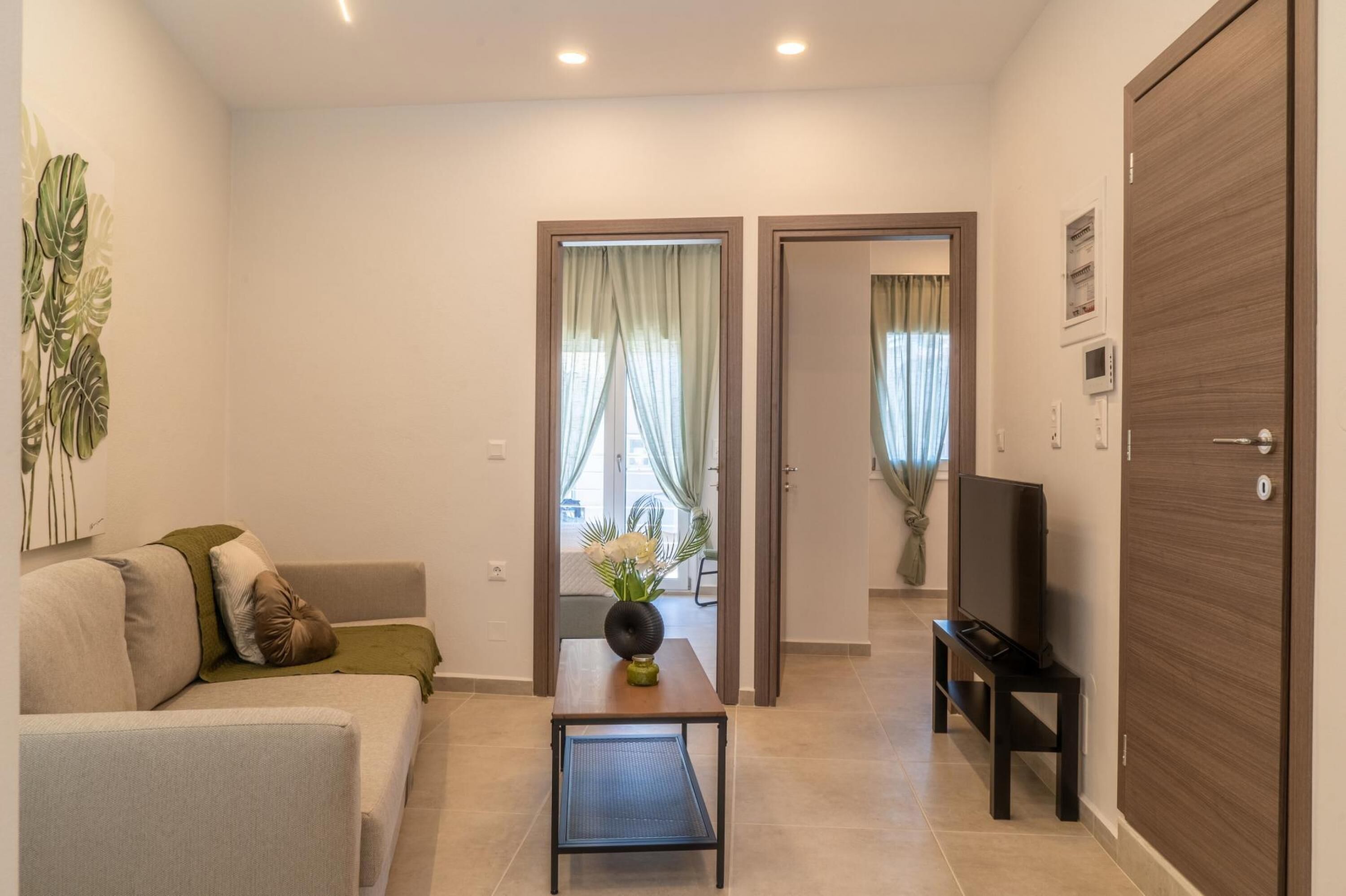 Un salon moderne avec un canapé, une table basse, un téléviseur posé sur un meuble et une porte donnant sur une autre pièce.