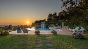 A swimming pool with lounge chairs and a small gazebo, surrounded by greenery and a view of the sunset. - Villa Ai Venti 8 Emma Villas (Massarosa)