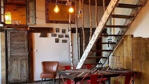 A rustic dining area with a wooden table, red chairs, and a staircase. - Gîte Chaleureux en Périgord Vert (Sarlande)