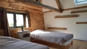 A bedroom with two beds, a nightstand with a plant, a window with curtains, and wooden beams on the ceiling. - Gîte Chaleureux en Périgord Vert (Sarlande)