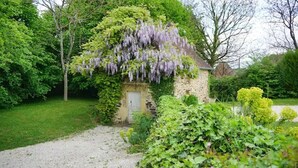 A stone cottage with a gravel path leading to it, surrounded by lush greenery and a wisteria-covered wall. - Gîte Chaleureux en Périgord Vert (Sarlande)