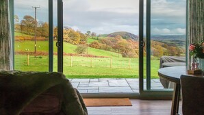 Ein Zimmer mit einer großen Schiebetür und einem herrlichen Blick auf ein grünes Feld, Bäume und Hügel.