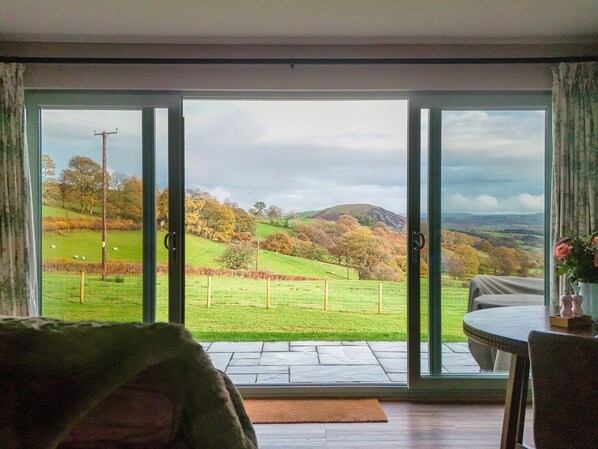 A room with a large sliding glass door leading to a scenic outdoor view of a green field, trees, and hills.