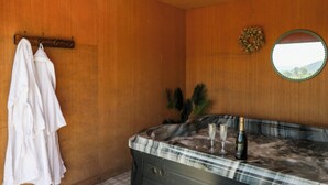 Ein Badezimmer mit Holzwänden, einer Marmortonne, einem Spiegel und zwei weißen Bademänteln, die auf einem Kleiderständer hängen.