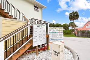 A menu board outside a building with a staircase leading to a door.