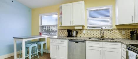 A compact kitchen with white cabinets, a dishwasher, and a countertop with a coffee maker.