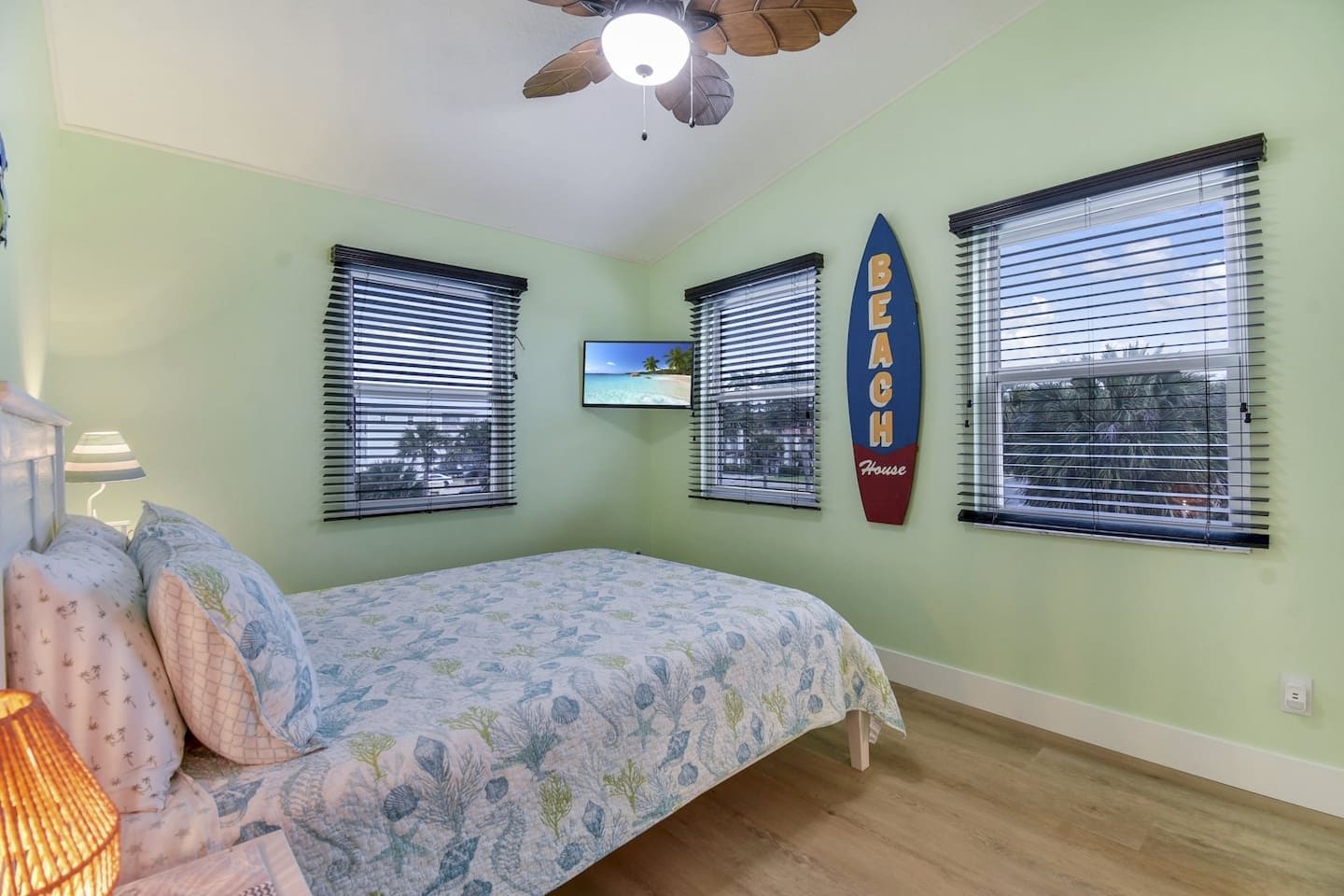 Un dormitorio con una cama, un ventilador de techo y un televisor en la pared.