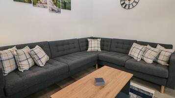 A modern living room with a grey sectional sofa, a wooden coffee table, and a wall clock.