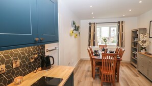 A modern kitchen with blue cabinets, a wooden dining table, and a window with curtains. - Eboracum (Hope Valley)