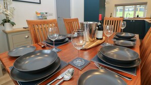 A dining table set with black plates, wine glasses, and cutlery, with a bottle of wine and a decorative vase on the table. - Eboracum (Hope Valley)