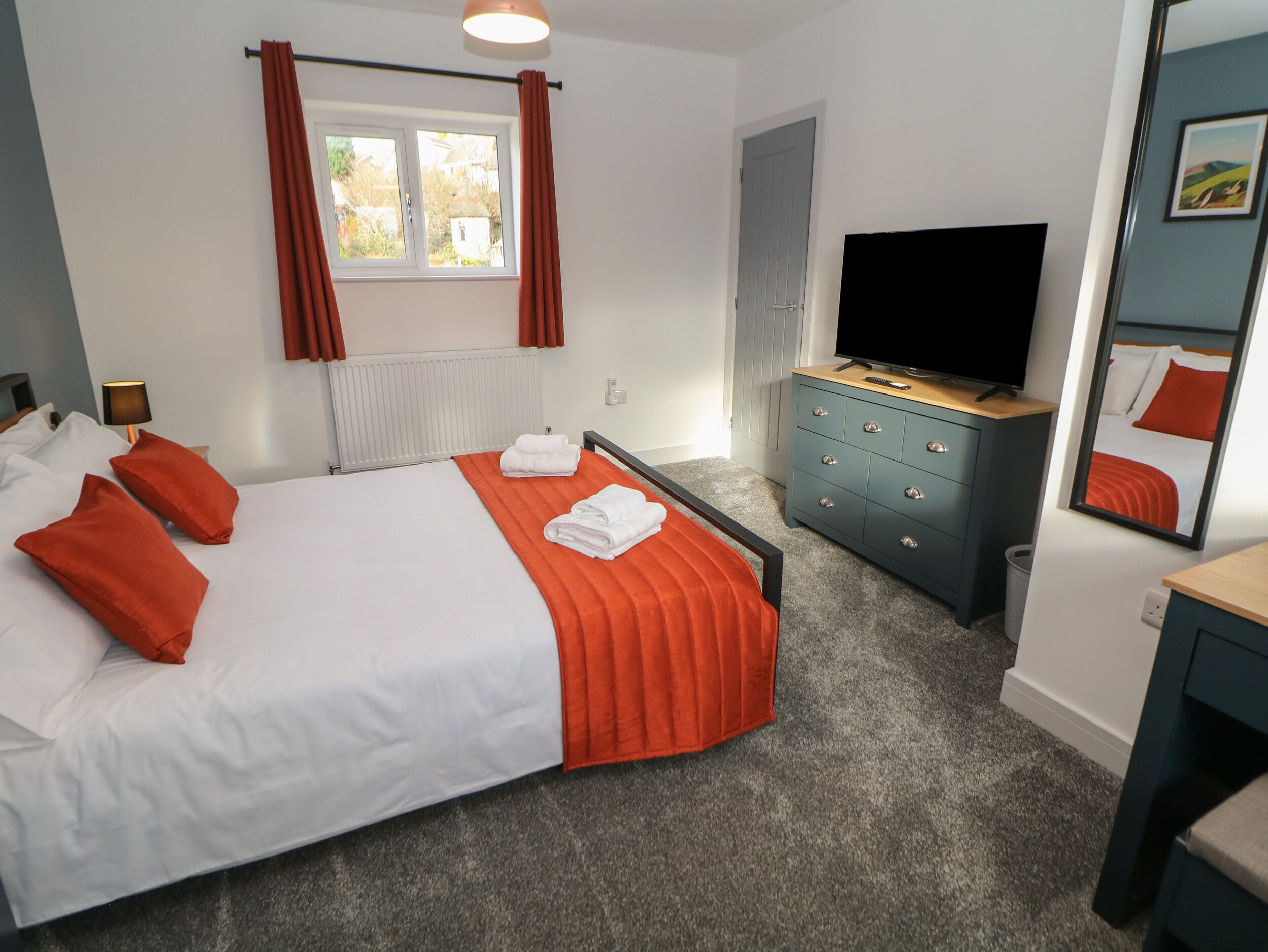 Habitación de hotel con cama, televisor, cómoda y ventana con cortinas.