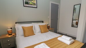 A neatly made bed with white and mustard bedding, a bedside lamp, and a folded towel on the bed. - Eboracum (Hope Valley)