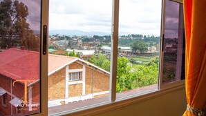 A view from a window with a curtain, overlooking a town with buildings and greenery. - TOKY Hôtel (Antsirabe)