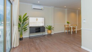A modern living room with a flat-screen TV, a potted plant, and a dining area with a table and chairs.