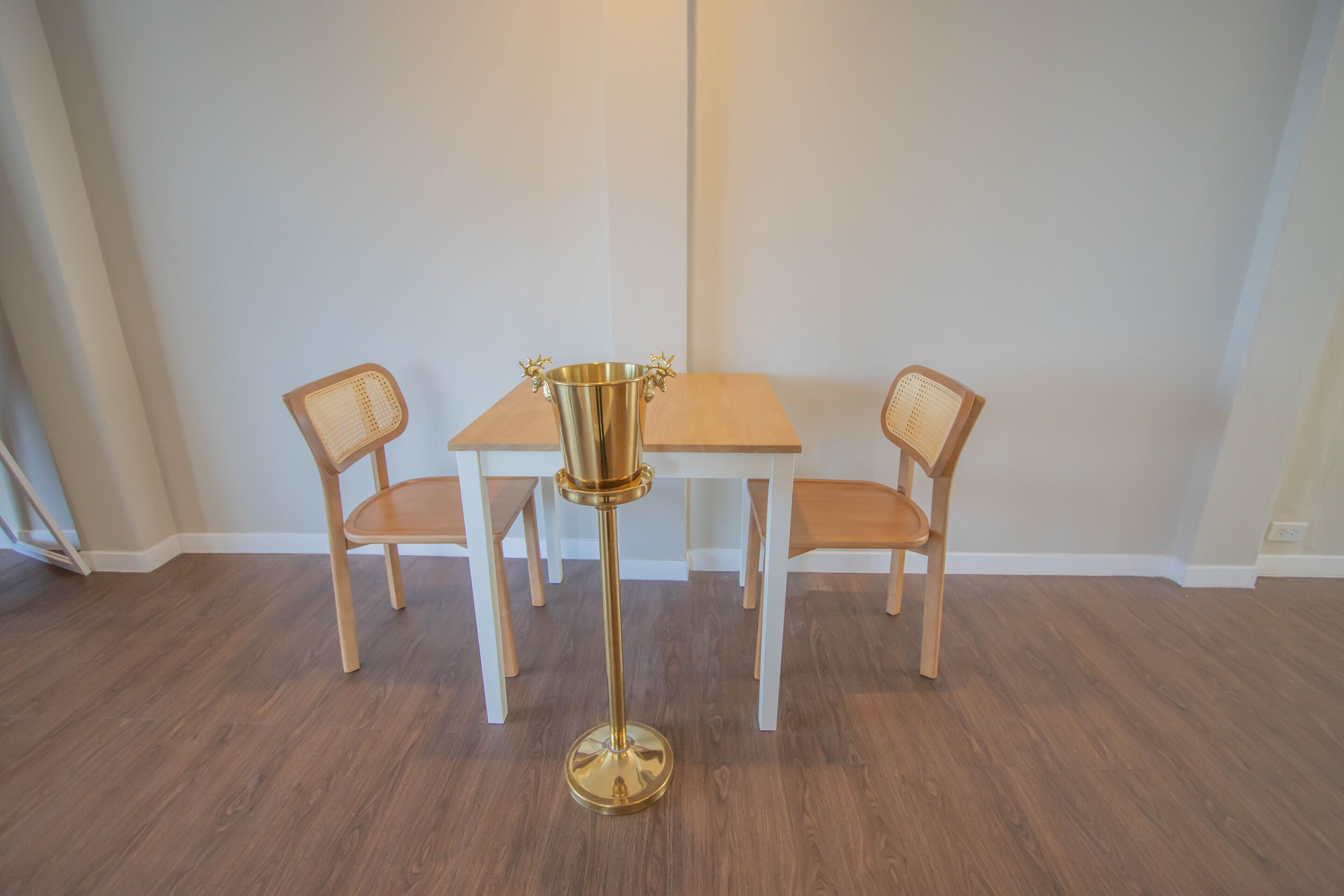 A dining area with a wooden table and two chairs, a gold floor lamp, and a white wall.