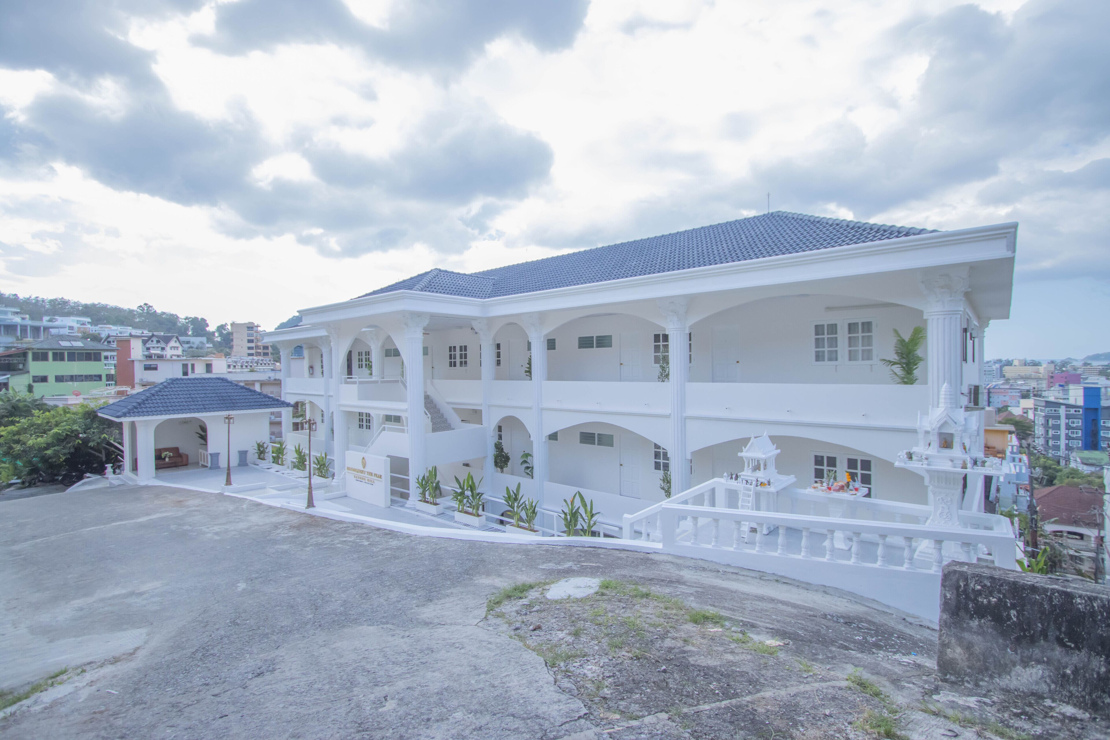 A multi-story building with a white facade and blue roof, featuring balconies and a central courtyard.