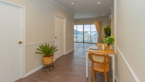 A hallway with a dining area, a potted plant, and a view through a window.