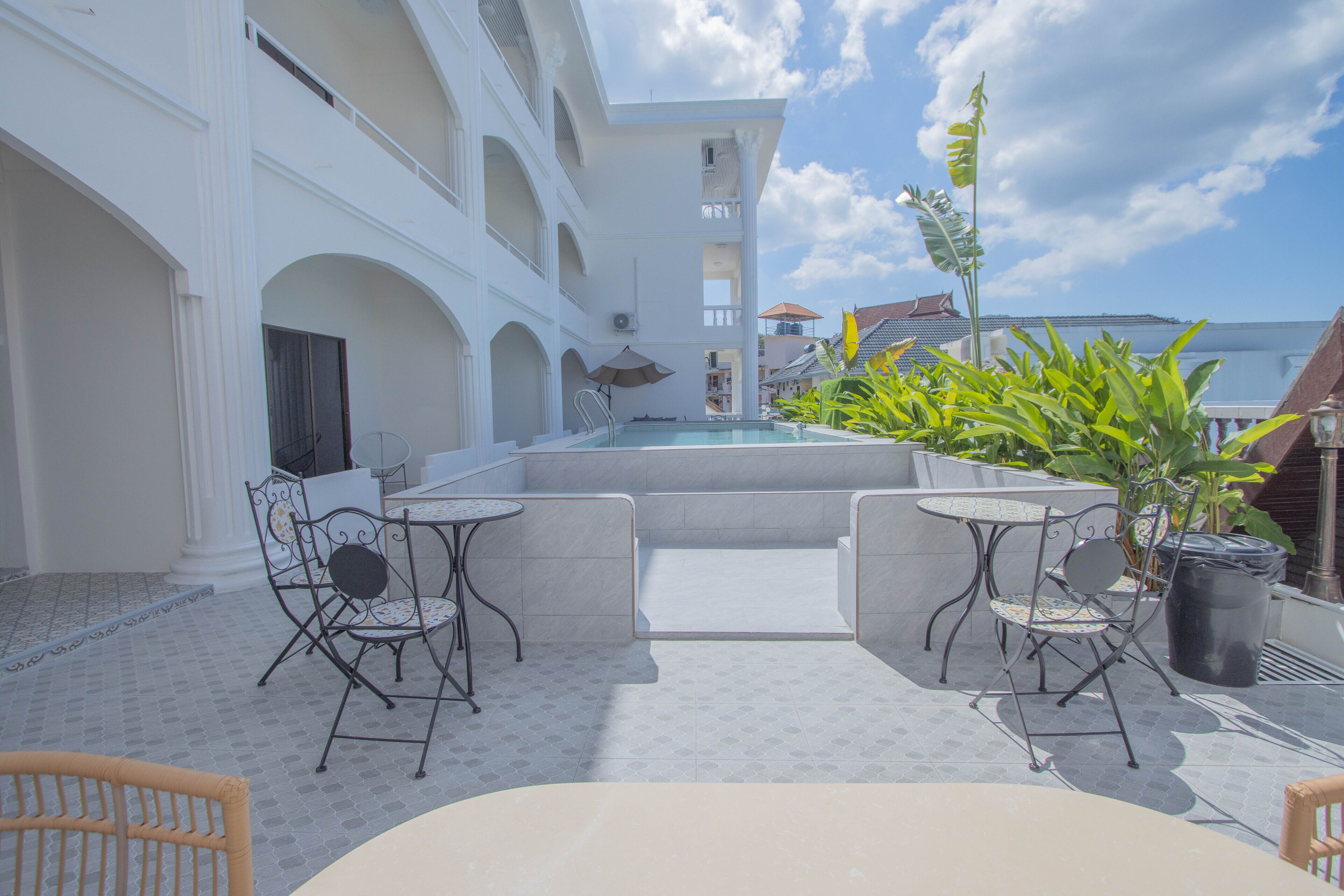 Un espace piscine aménagé sur le toit, avec un coin salon comprenant deux chaises et une table, entouré de plantes en pot et offrant une vue sur un ciel dégagé.