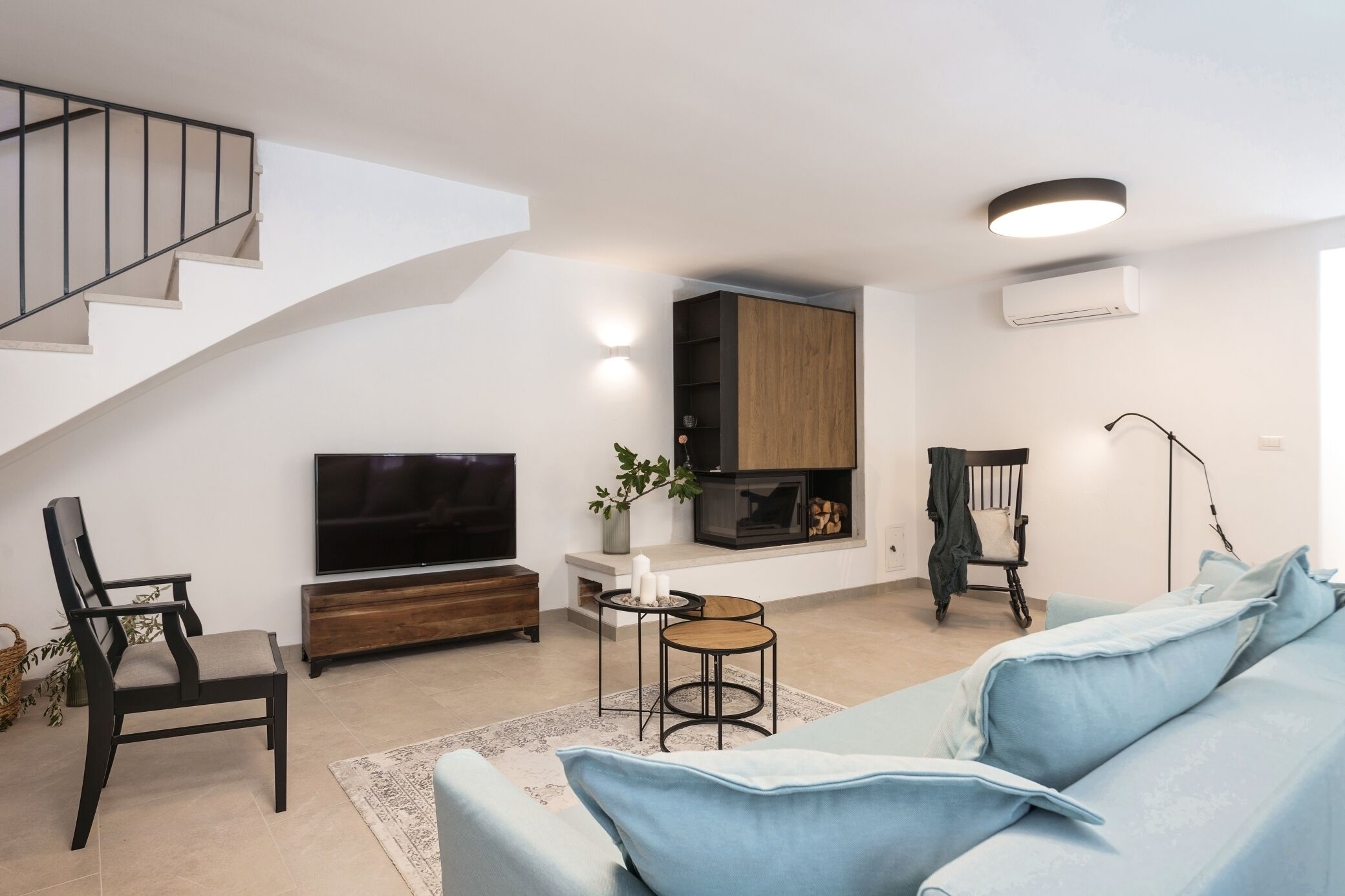 Un saló modern amb escala, televisió plana, llar de foc, sofà i zona de menjador.