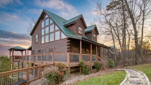 A log cabin with a porch and a deck, surrounded by a stone pathway and greenery. - Misty Mountain by AvantStay | Hot Tub, Mountain Views, Theater, Pool Table (Sevierville)
