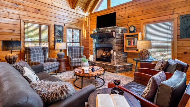 A cozy log cabin interior with a fireplace, comfortable seating, and large windows. - Misty Mountain by AvantStay | Hot Tub, Mountain Views, Theater, Pool Table (Sevierville)